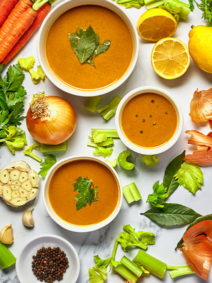 Bowls of bone broth with fresh vegetables and herbs, highlighting natural calcium-rich ingredients.