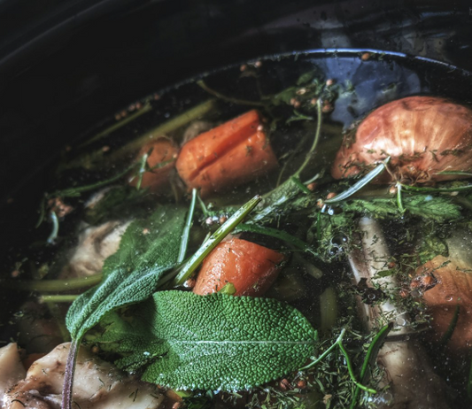 bone broth simmering with fresh herbs, carrots, onions, and chicken bones for gut health and immunity.